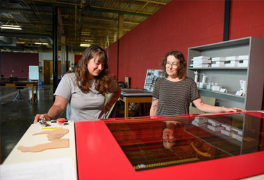 An student and Professor Sharon Massey use a large Rabbit Laser Cutter to cut matrix dies in the STEAM Shop.