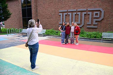 a parent taking a photo of four students standing in front of the IUP logo at the library
