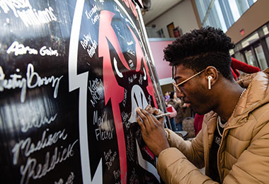 a young man using a silver sharpie marker to sign his name to a large sign with the IUP crimson hawk logo on it