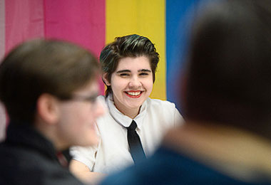 a student smiling towards the camera while sitting in front of a rainbow flag