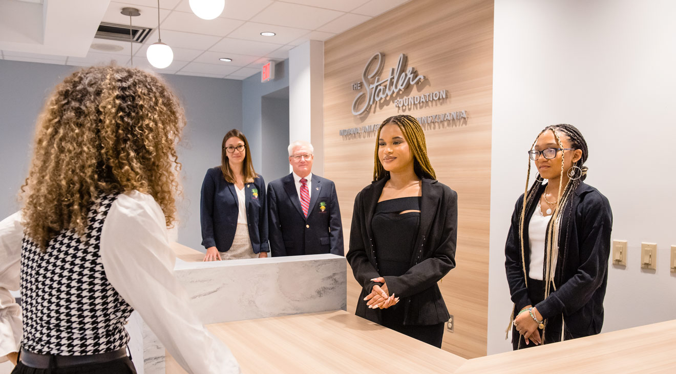 Faculty members Nicole Buse and Stephen Shiring watch as, from left, Tezmionah Jordan, Ousmane Diallo, and Kayla Cardwell use the simulated hotel front desk
