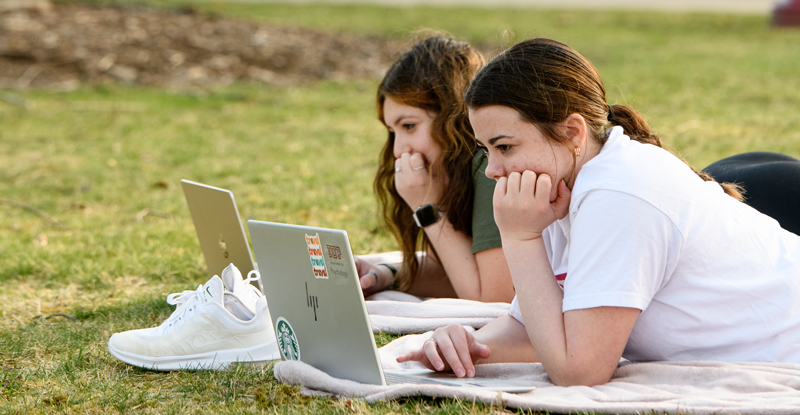 two female students studying in the oak grove on laptops