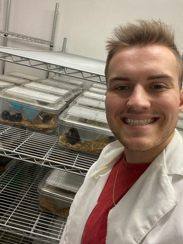 Nickolas Vasil posing in front of a rack containing various lab mice