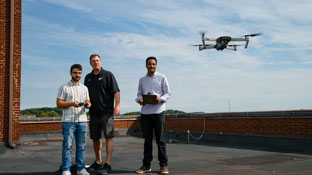 faculty with 2 students on a rooftop flying a drone