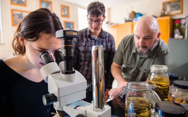 Josiah Townsend and two students looking at samples under a microscope in a lab