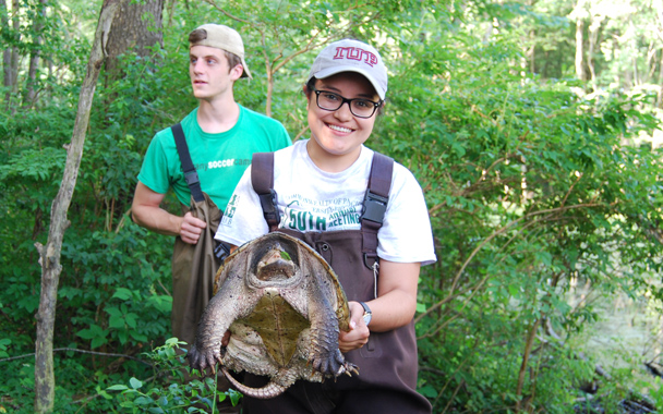 a female student holds a tortoise with another student standing behind her