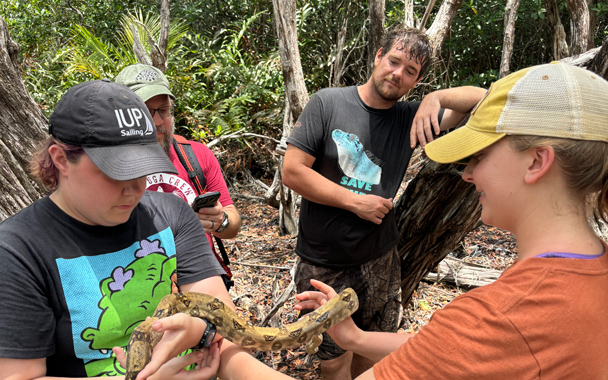 a small group of students hold and examine a snake in a jungle