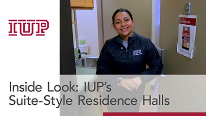 a young woman smiling for the camera while opening a door to a dorm building