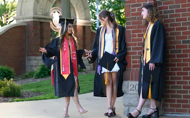 Three students standing in the oak grove wearing their cap and gowns