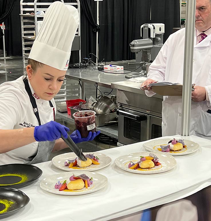 Chef Reed plating cheesecake under a judge's watchful eye