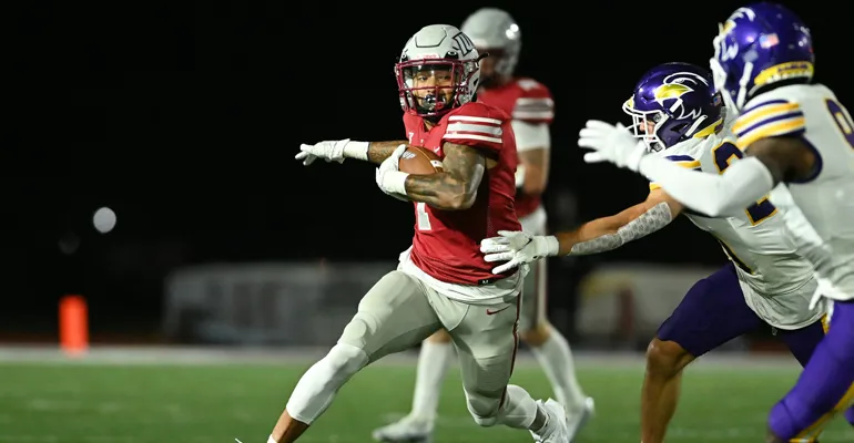 An IUP football player running the ball up field against two opponents