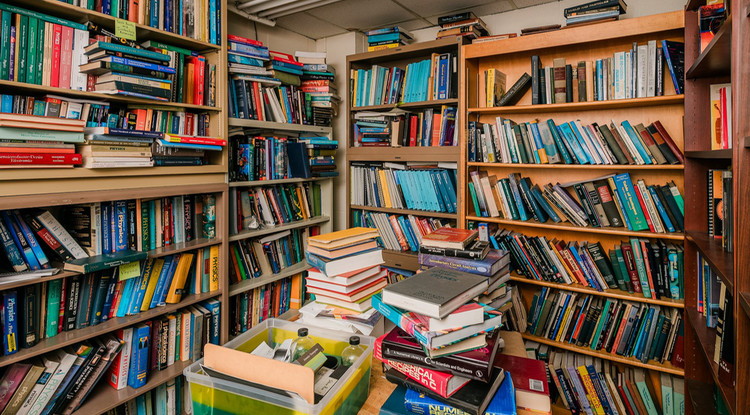 a small room covered in full bookshelves with additional books scattered on a small table in the middle