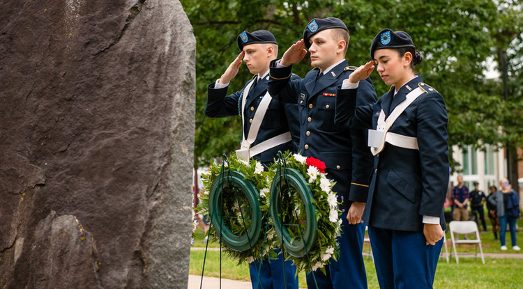 three students saluting a memorial