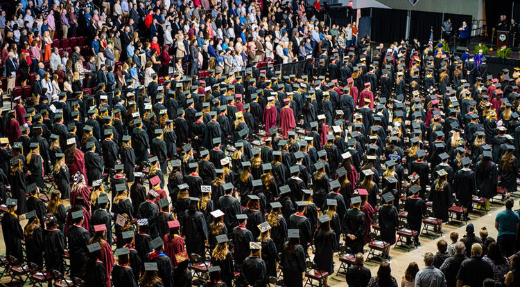 a large group of students in cap and gown facing a stage during a commencement ceremony