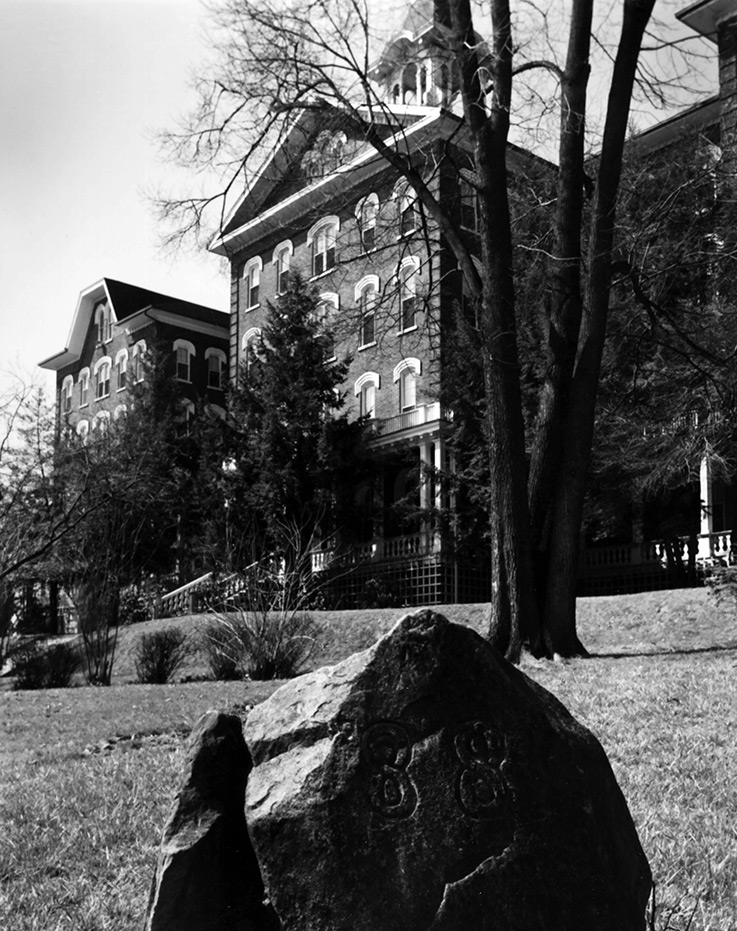 A rock engraved with “’88” is in the foreground, with John Sutton Hall behind it