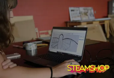 an overhead shot of a person using a computer.  The STEAMSHOP logo is on the bottom right