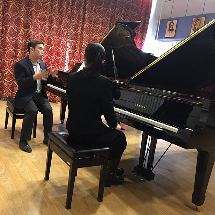 Henry Wong Doe talking with student in front of piano in China Henry Wong Doe talking with student in front of piano in China